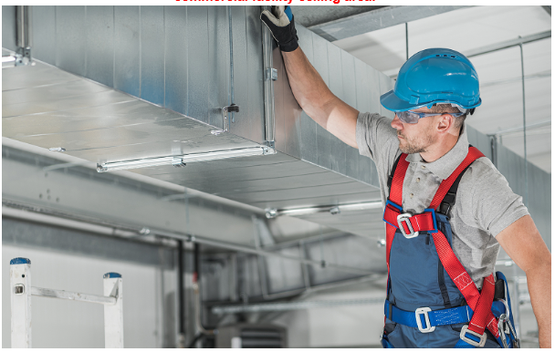 A technician performing high dusting with safety gear in a commercial facility ceiling area.